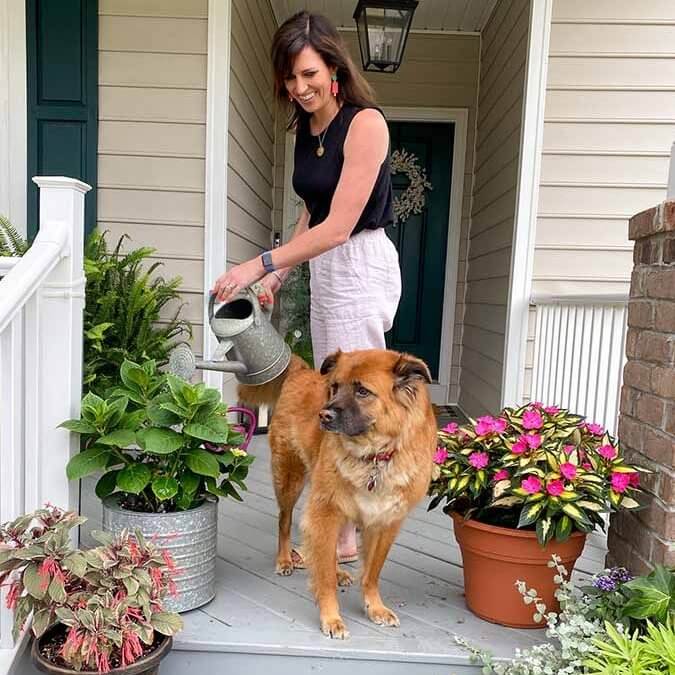Woman tending her porch plants with a reddish/gold dog