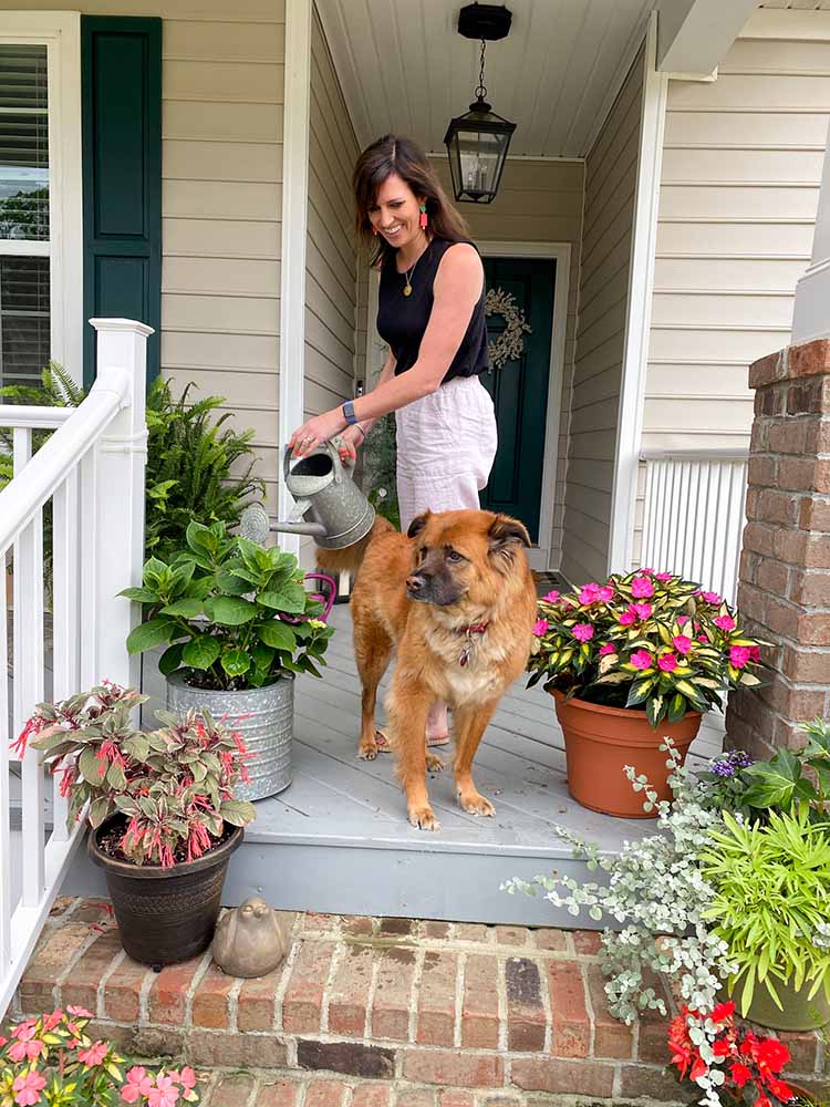 Woman tending her porch plants with a reddish/gold dog