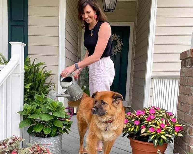 A woman watering plants on her porch with her pup